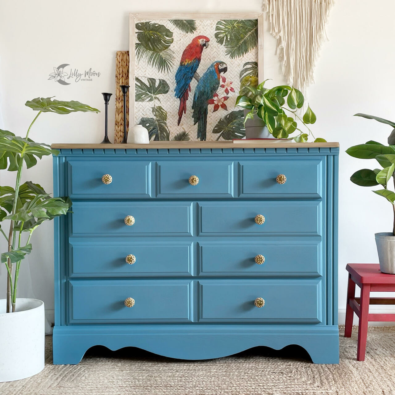 Teal blue painted dresser in the color Tide Pool with boho wall decor, house plants, tropical parrot art and a red stool
