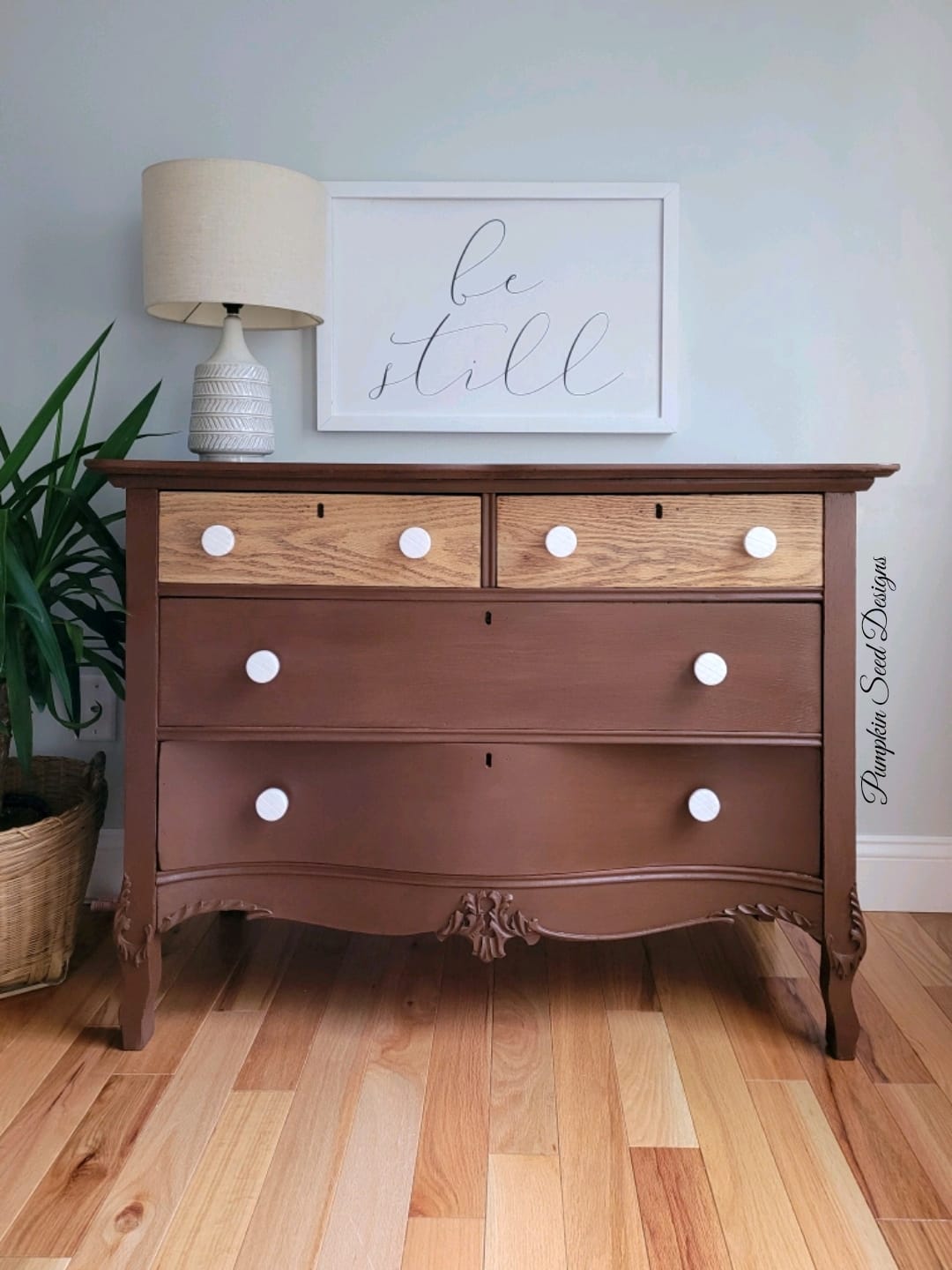 Chocolate brown painted antique dresser. Be still wall art and white lamp.